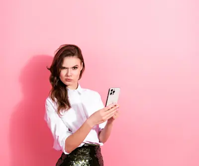 Mujer desconfiada mira de reojo mientras sostiene el celular sobre fondo rosa