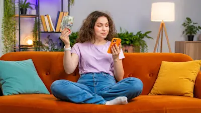 Mujer en el sillón con billetes de dólar en una mano y el celular