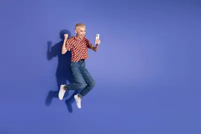 Mujer salta feliz con el celular en la mano sobre fondo azul