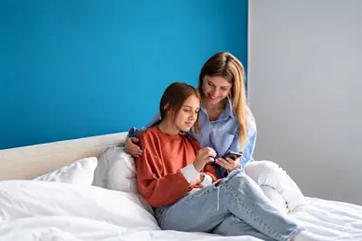 Madre e hija adolescente miran juntas el celular sentadas en la cama