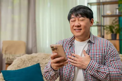 Hombre aliviado con la mano en el pecho mira el celular en su casa