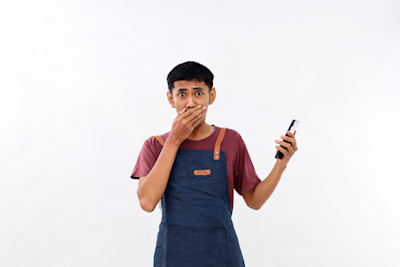 Comerciante con delantal se tapa la boca sorprendido mientras sostiene el celular