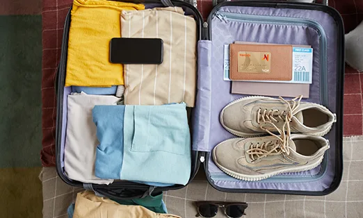 Imagen de una valija con ropa dentro, un pasaje de avión y una tarjeta Naranja Visa