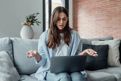 Mujer confundida en el sillón frente a una notebook revisa una oferta de trabajo