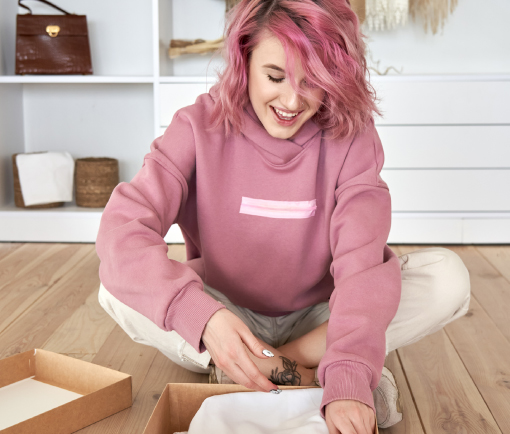 Mujer joven sentada sobre en el piso de madera abriendo un paquete.