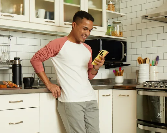 Hombre en su cocina con el teléfono celular en su mano.