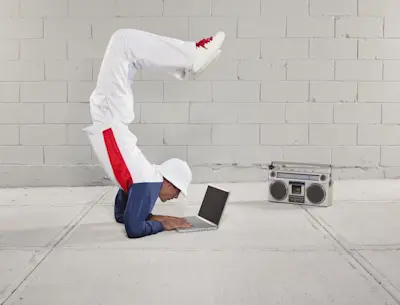 Joven hace una pirueta de breakdance mientras usa una notebook en el piso