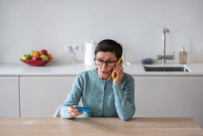 Mujer con anteojos habla por teléfono mientras sostiene una tarjeta en la cocina
