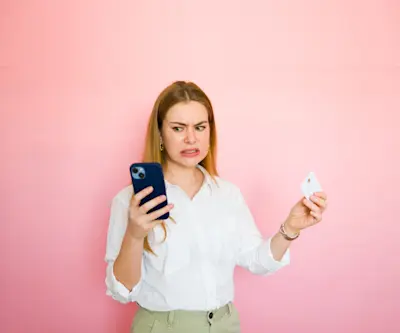 Mujer desconfiada sostiene el celular y una tarjeta sobre fondo rosa