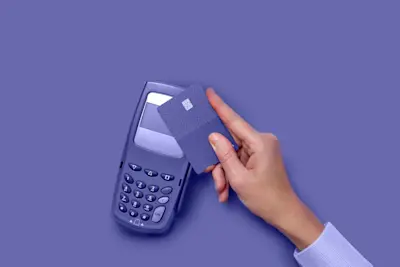 Mano acerca una tarjeta contactless a una terminal de pago sobre fondo violeta