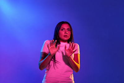 Mujer asustada muestra las palmas en señal de rechazo bajo luces violetas