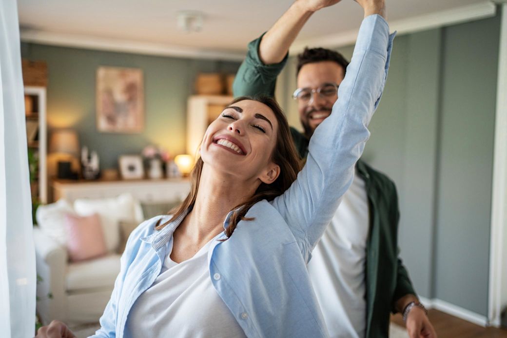 Ein junges, fröhliches Paar tanzt zusammen zuhause im Wohnzimmer