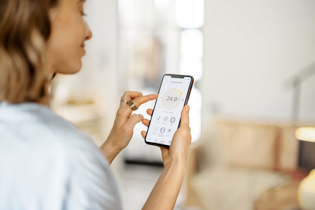 Frau passt in einer Smart-Home-App auf ihrem Handy die Zimmertemperatur an.