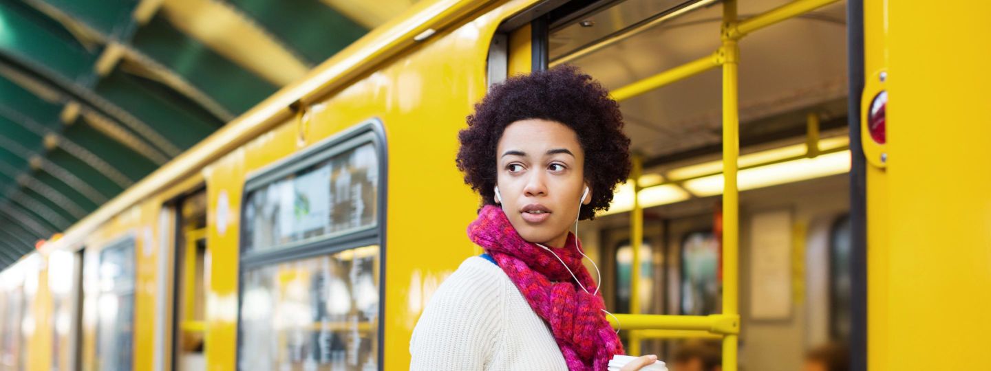 Weibliche Person mit Smartphone und Kopfhörern steigt in gelbe Berliner Straßenbahn.