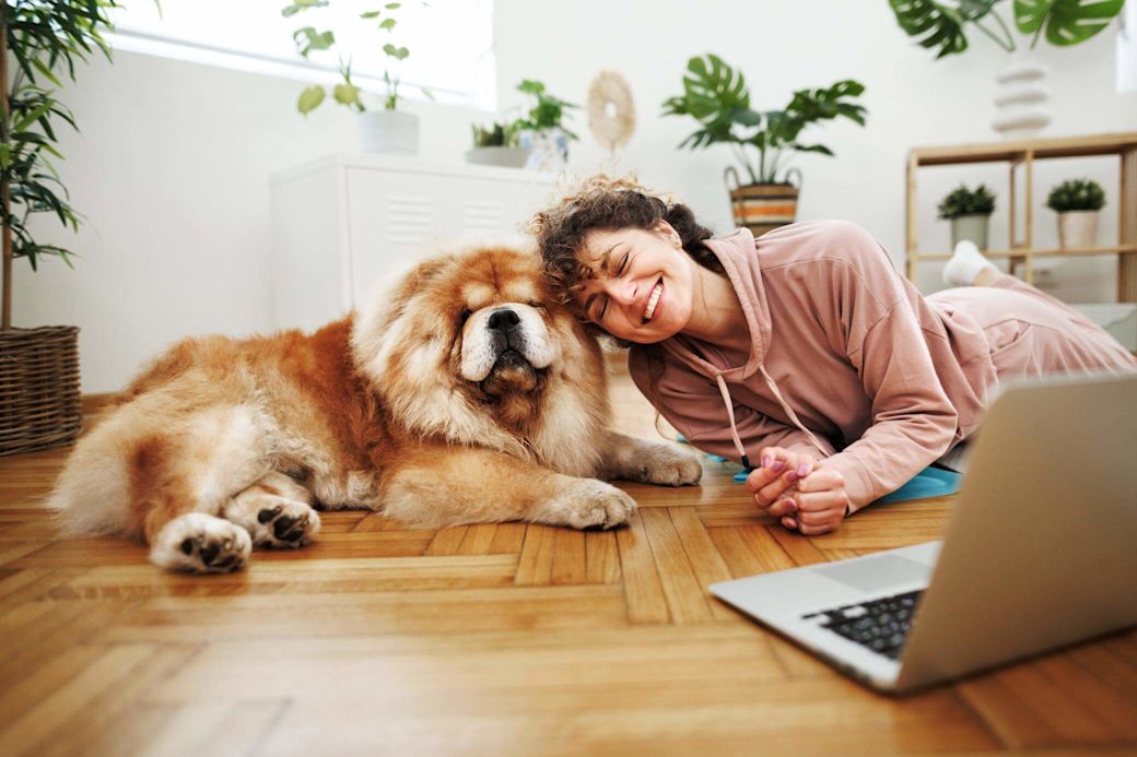 Lachende Frau sitzt mit ihrem Hund auf dem Boden