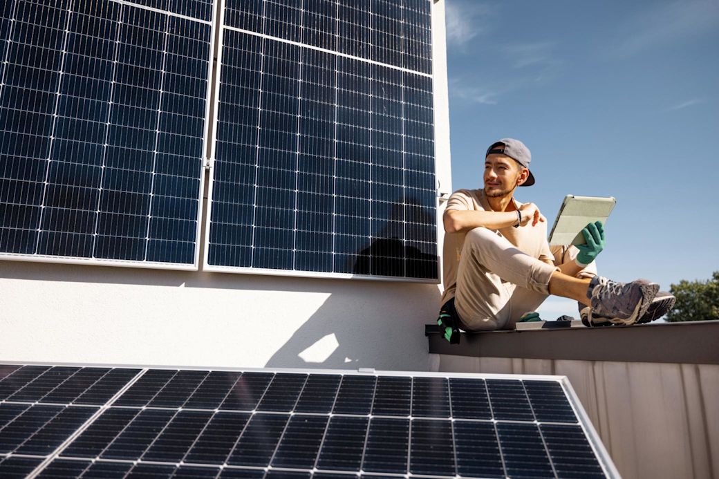 Mann prüft Solarmodule auf einem Dach mit Tablet