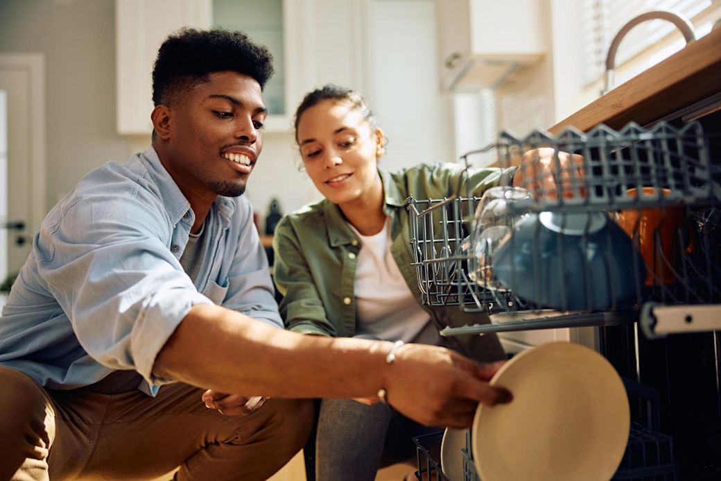 Frau und Mann räumen Geschirr in die Spülmaschine