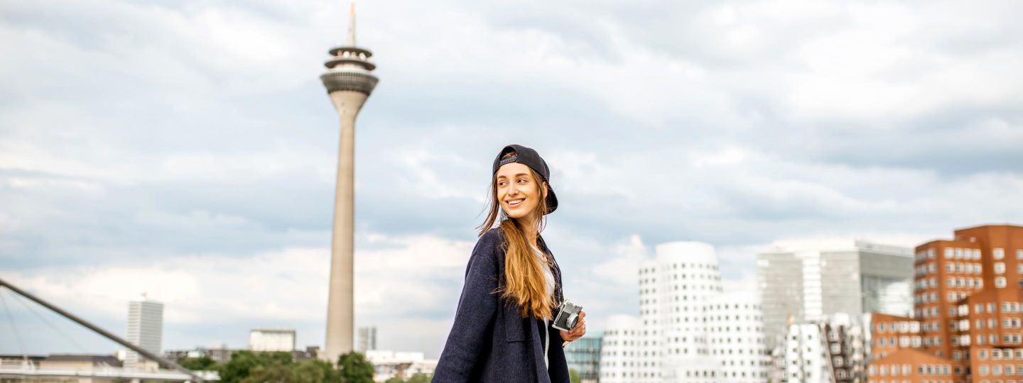 Junge Frau mit roter Tasche in der Hand und Cap auf dem Kopf am Mediahafen in Düsseldorf