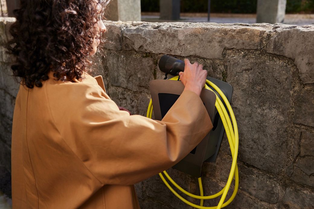 Frau hängt das Ladekabel fürs E-Auto über die Wallbox