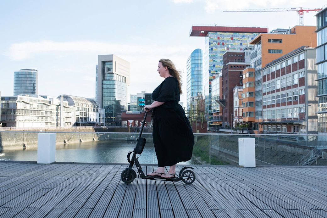 Frau mit schwarzem Kleid rollt auf E-Scooter durch den Rheinhafen in Düsseldorf