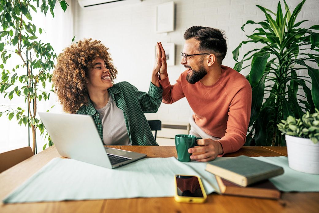 Mann und Frau mit Laptop bei der Arbeit geben sich ein High Five