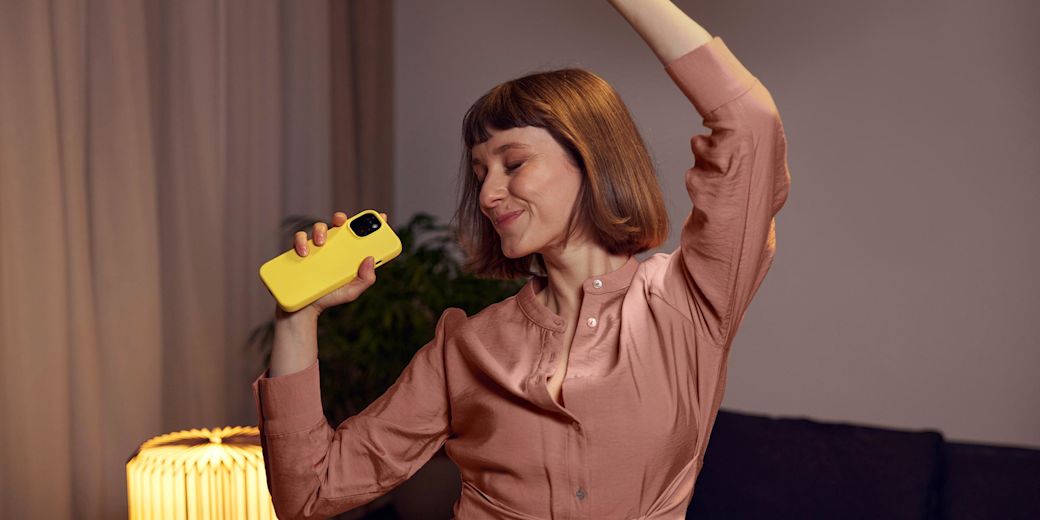 Frau tanzt mit Smartphone im Wohnzimmer.
