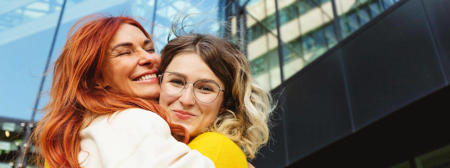 Zwei glückliche Frauen, die sich vor einem Gebäude umarmen.