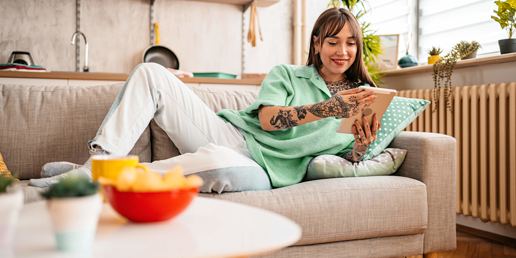 Junge Frau auf dem Sofa steuert mit dem Tablet ihre Smart-Home-Geräte