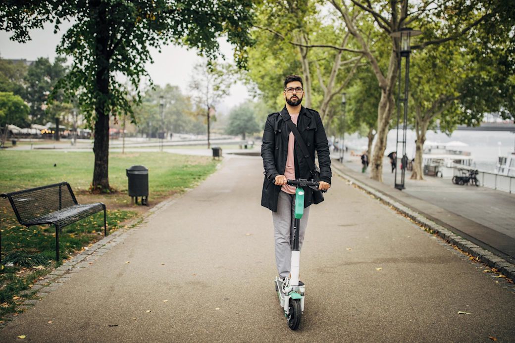 Mann mit E-Scooter fährt durch den Stadtpark.