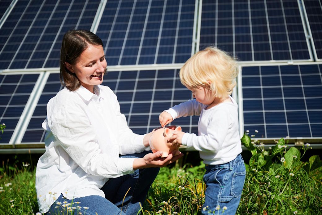 Frau mit Kind und Sparschwein vor einer Solaranlage
