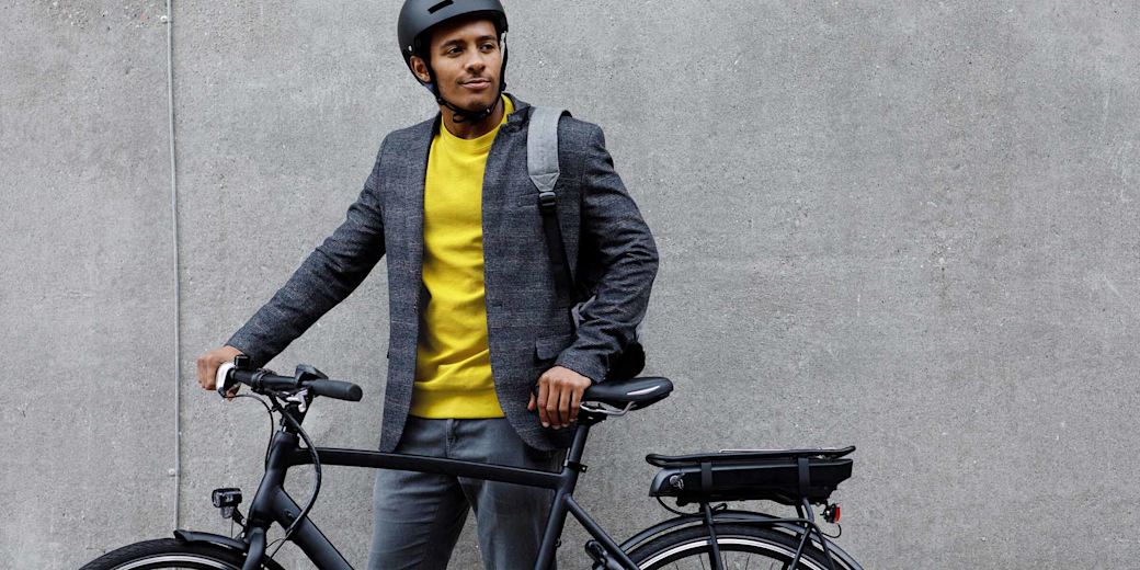 Mann steht mit seinem E-Bike Fahrrad vor einer grauen Wand.