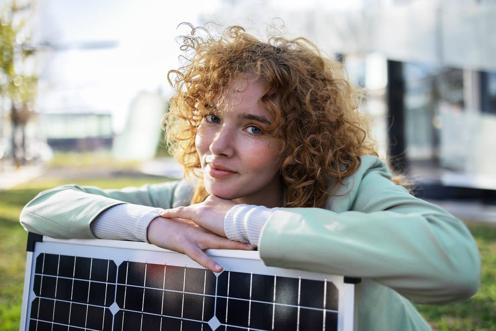 Frau mit Locken lehnt auf einem Solarmodul im Garten 
