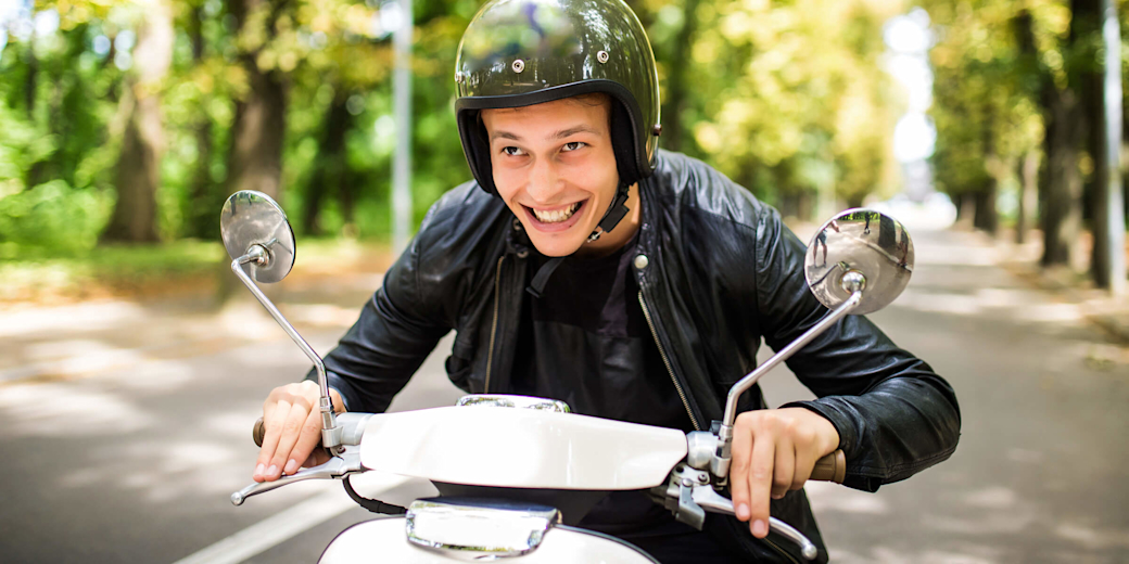 Junger Mann fährt Elektroroller durch Baumallee.