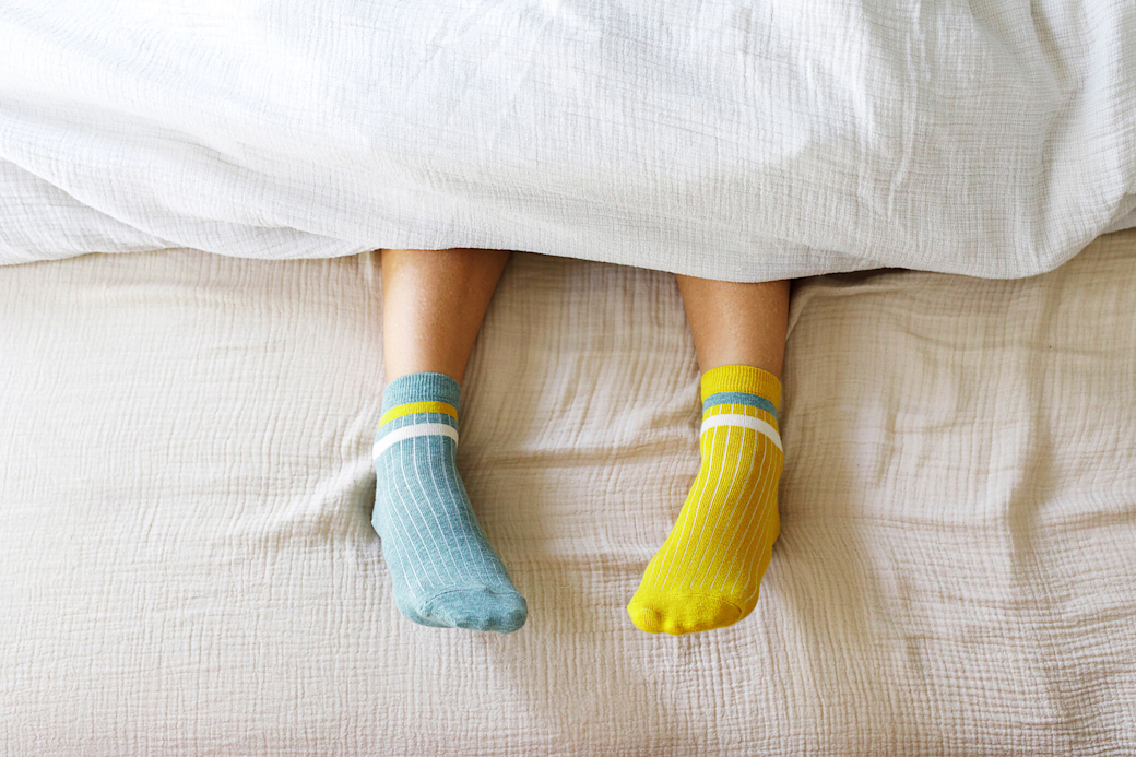 Zwei Füße unter der Bettdecke in bunten Stricksocken.