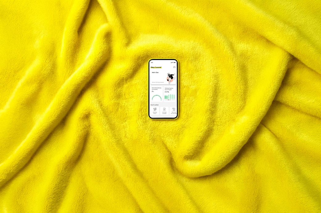 Ein Smartphone auf warmer, gelber Decke zeigt Bildschirm für Gastarif in der Yello App - KI generiert