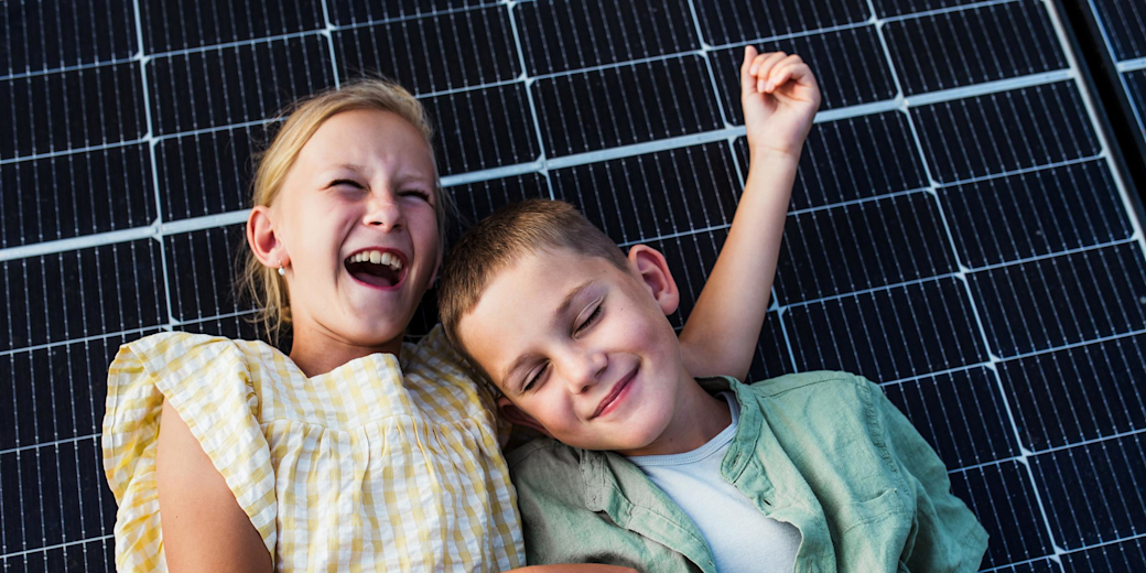Mädchen und Junge liegen fröhlich auf einem Solarpanel und lachen.