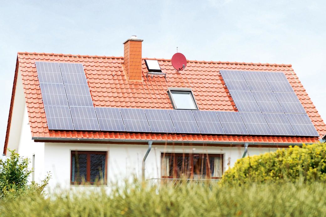 Haus mit einer Solaranlage auf dem Dach hinter einer Hecke 