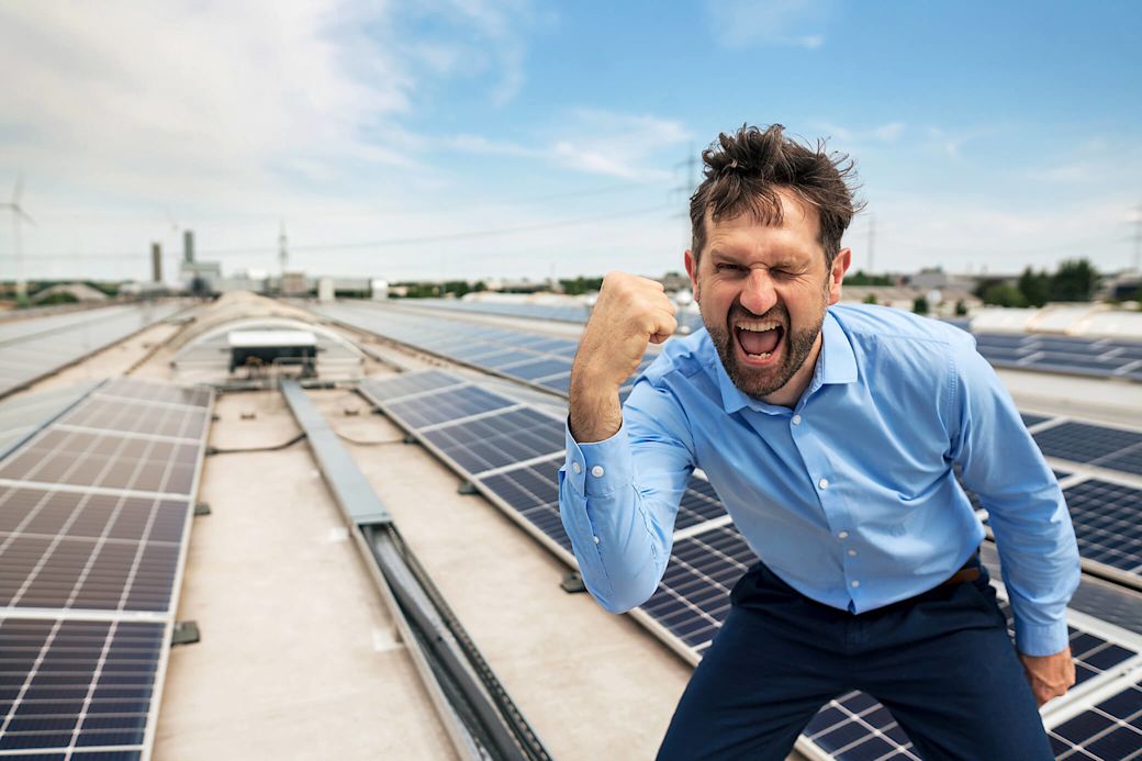 Ein Mann steht jubelnd auf einem Solar Dach