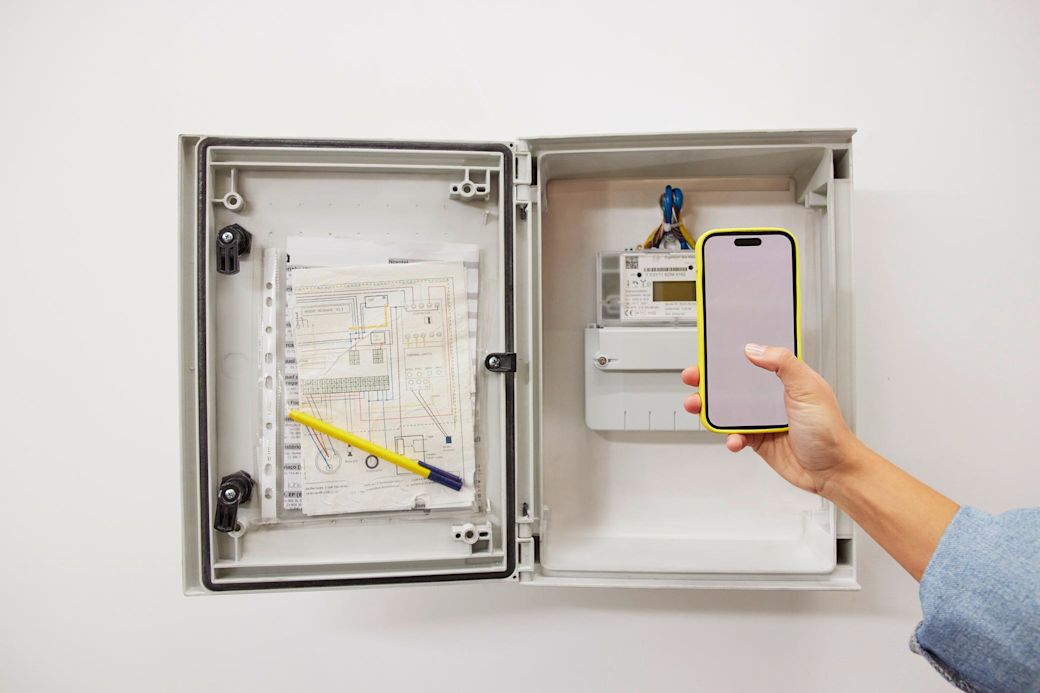 Frau liest mit gelbem Handy in der ihren Stromzähler ab