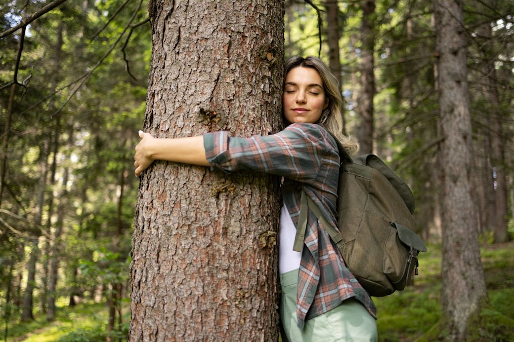  Frau umarmt mit geschlossenen Augen einen Baum in einem Wald
