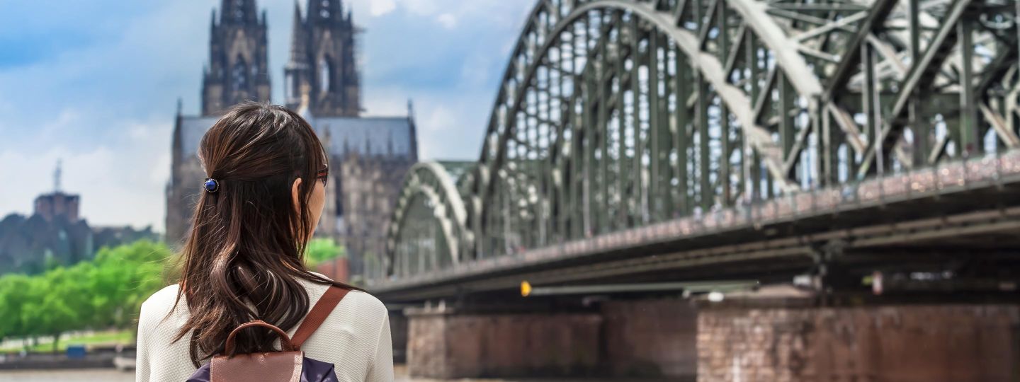 Eine Frau am Rhein schaut auf die Hohenzollernbrücke mit Kölner Dom