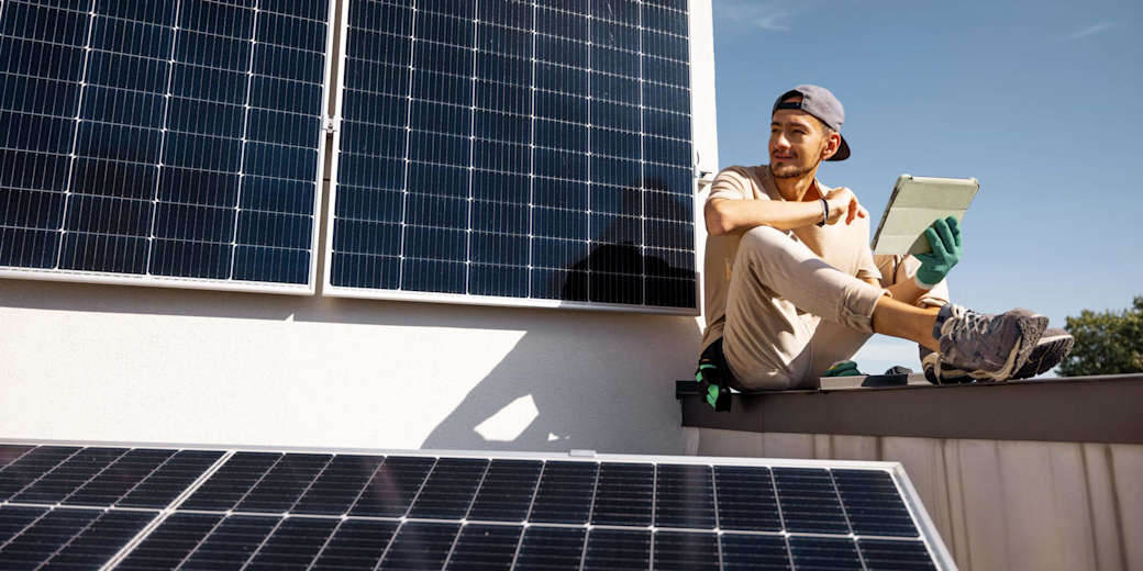 Mann prüft Solarmodule auf einem Dach mit Tablet.