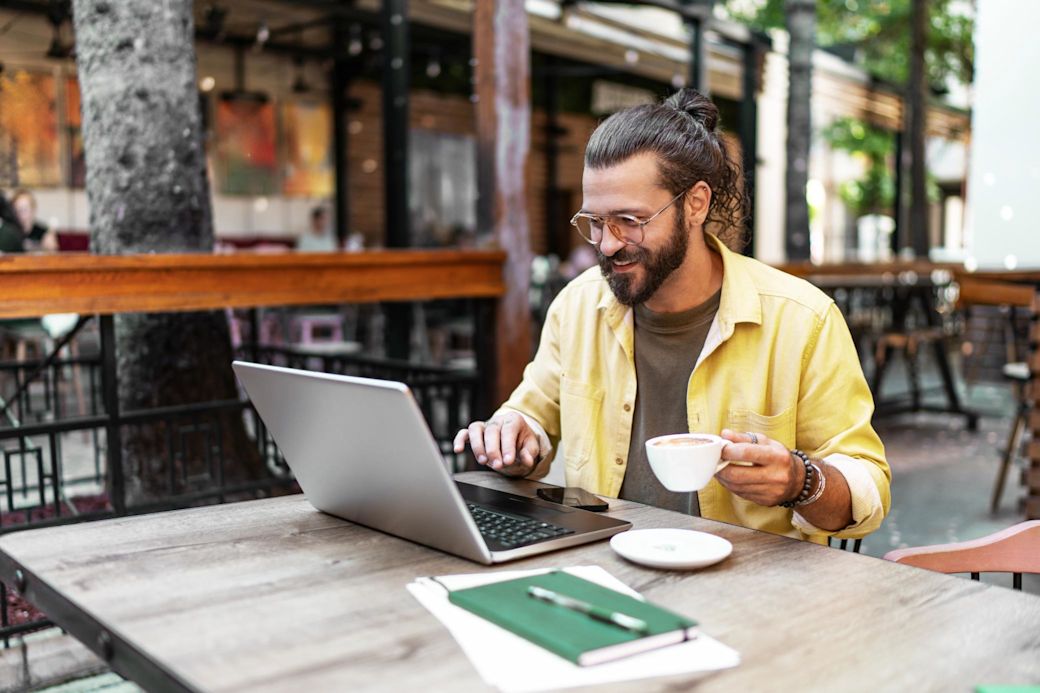 Junger Mann arbeitet in einem Café während sein E-Auto lädt