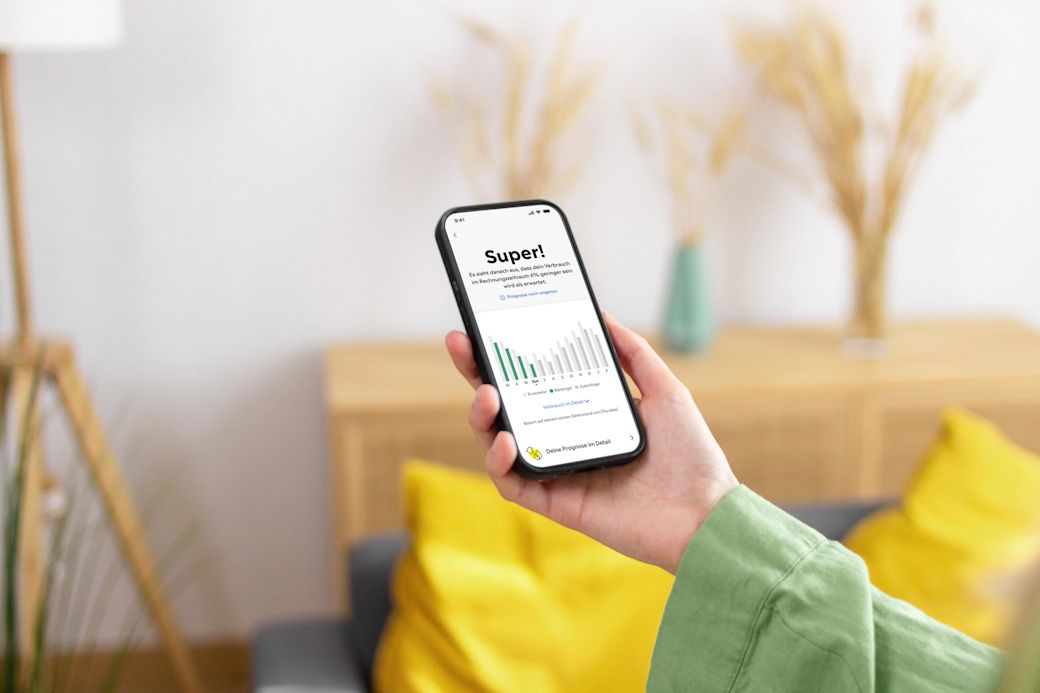 Hand einer Frau hält ein Handy mit Yello App und Screen mit Verbrauchsverlauf im grünen Balkendiagramm