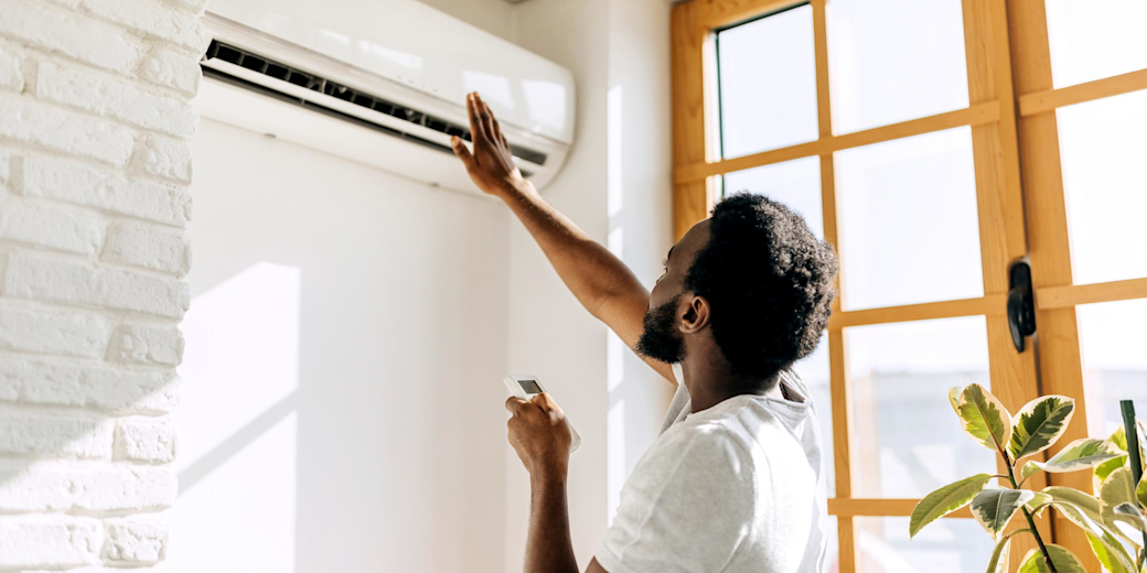 Mann in weißem T-Shirt und Fernbedienung prüft den Luftzug seiner Klimaanlage