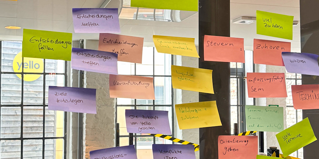 Ein Foto von bunten, beschriebenen Post-its an einer Glaswand