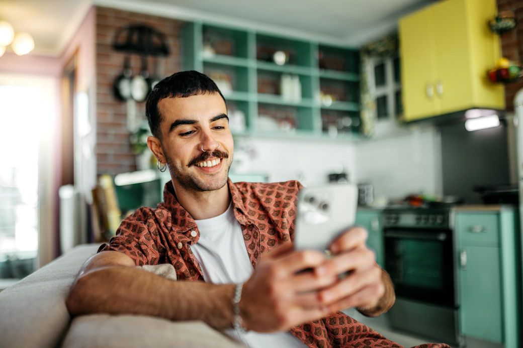 Ein Mann mit Handy sitzt auf der Couch und im Hintergrund ist eine grüne Küche
