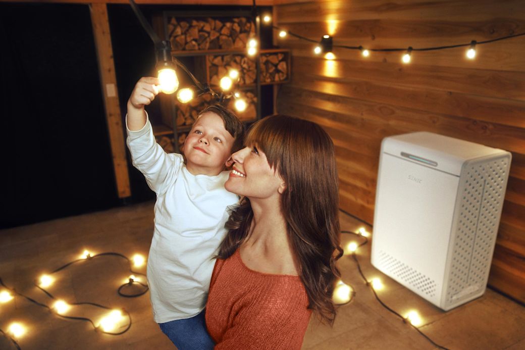 Mutter hält Kind, das mit Lichterkette spielt. Im Hintergrund ein Stromspeicher