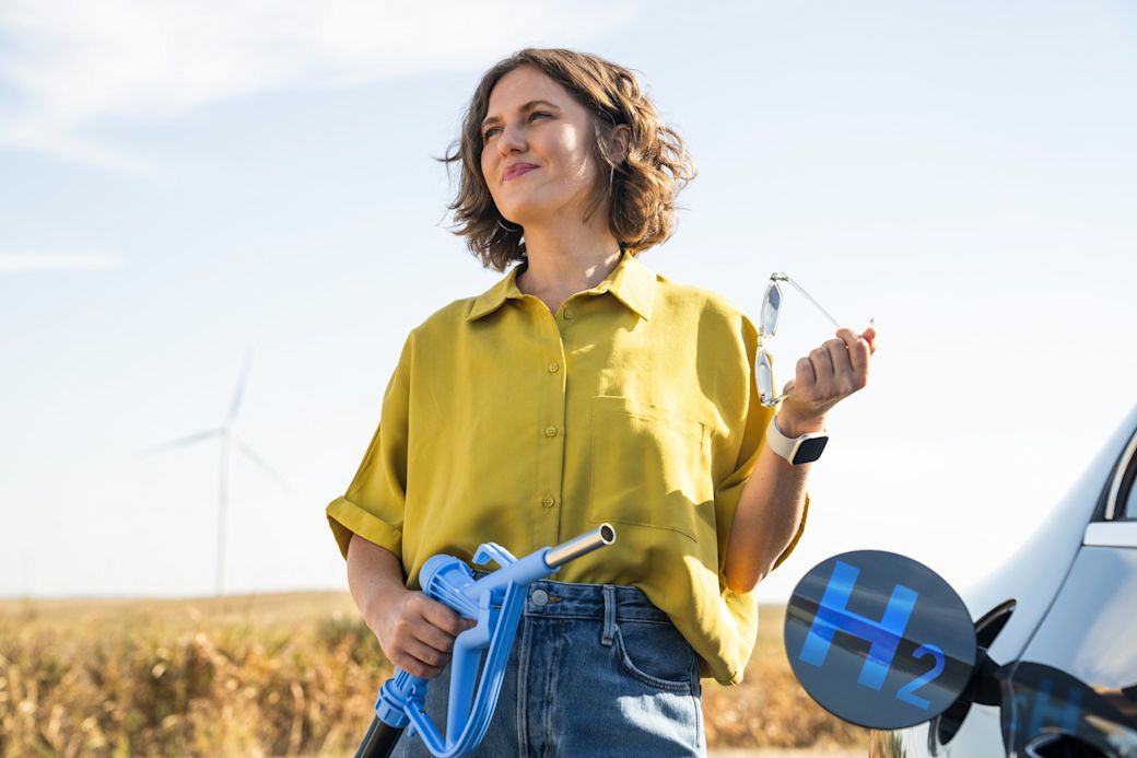 Frau mit Sonnernbrille in der Hand tankt ihr Auto mit Wasserstoff