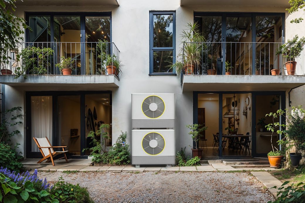 Zwei Wärmepumpen in einem grünen Hinterhof vor Haus mit Terrasse und Balkon